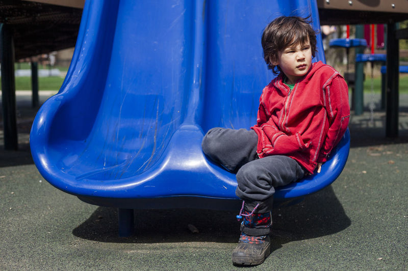 Thoughtful boy looking away while sitting on slide at playground during sunny day