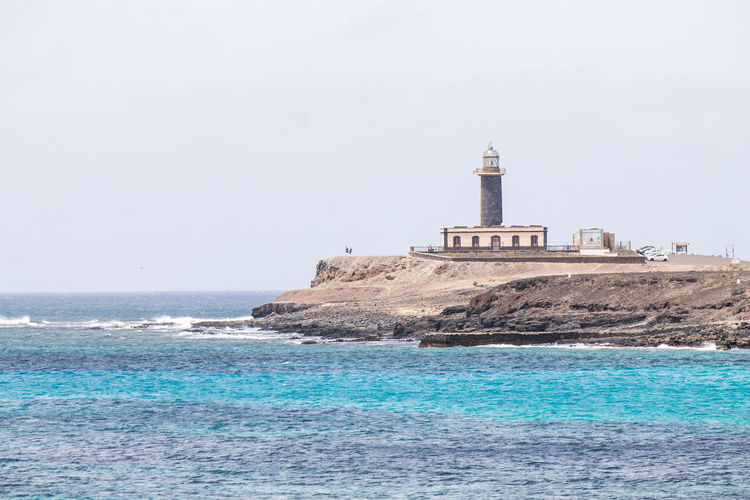 Lighthouse by sea against clear sky