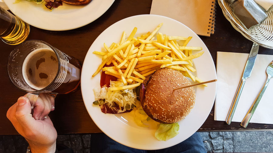 Cropped image of person having burger and beer on restaurant table