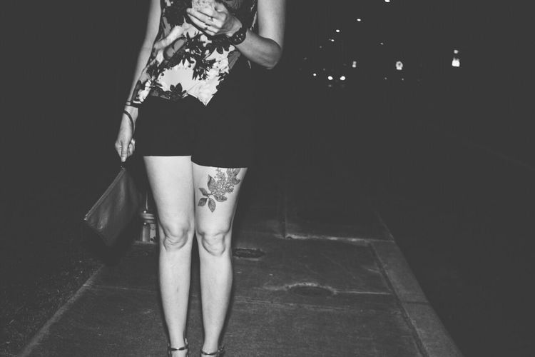 Midsection of woman with tattoo on thigh standing at sidewalk