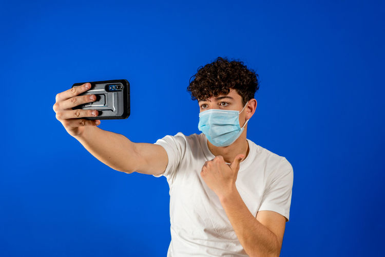 Young man photographing while standing against blue background