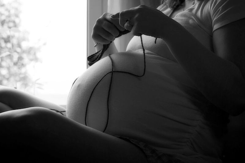 Midsection of pregnant woman knitting at home
