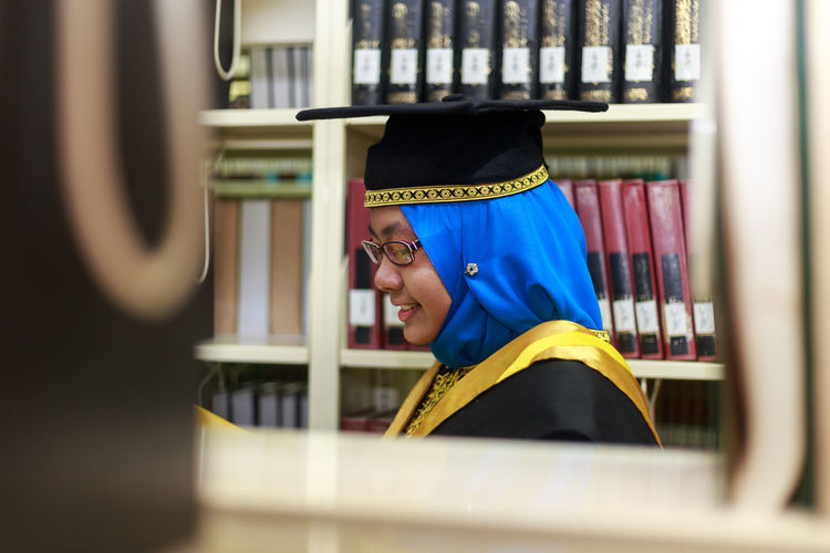 Young woman wearing graduation gown in library