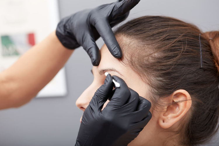 Cropped hands of beautician treating woman permanent eyebrow