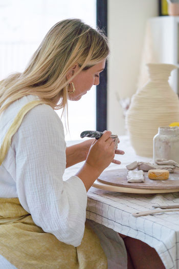 Female pottery artist making a vase in her home studio