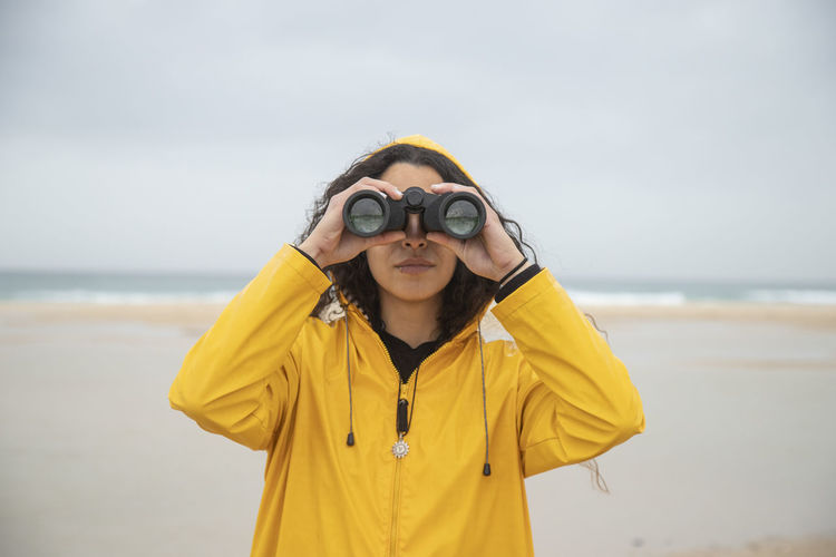Woman using binoculars while standing at beach
