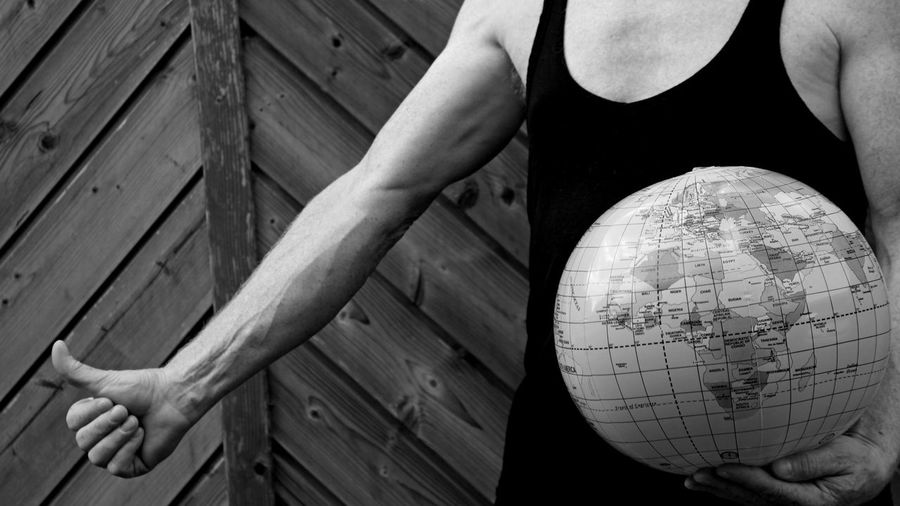 Midsection of man with globe gesturing while standing against wooden wall