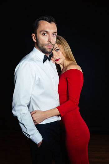 Portrait of elegant couple standing against black background