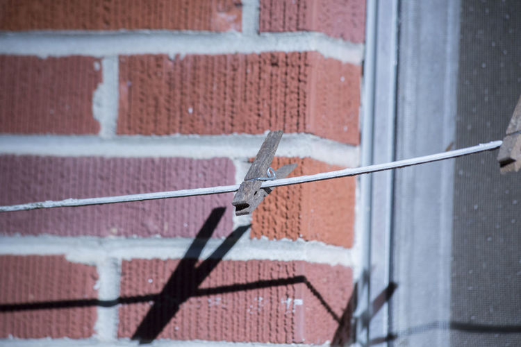 Single clothespin hanging in front of a red brick building and part of a window in the background