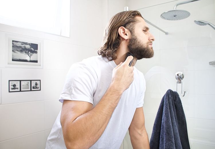 Young man shaving beard at domestic bathroom