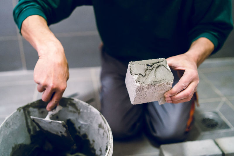 Low section of male worker applying cement on brick at home