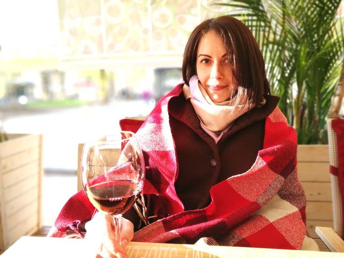 Portrait of young woman in warm clothing having wine while sitting at home