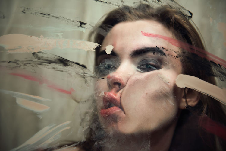 Close-up portrait of woman pressing her face on glass window