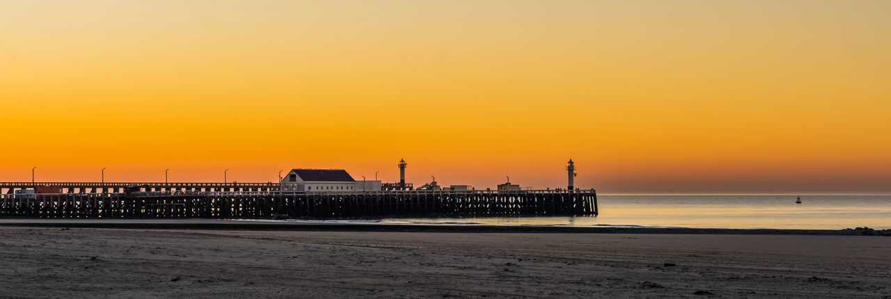 Silhouette pier on beach against orange sky