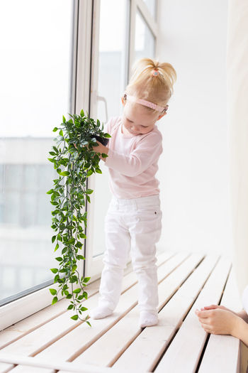 Girl holding plant by near window