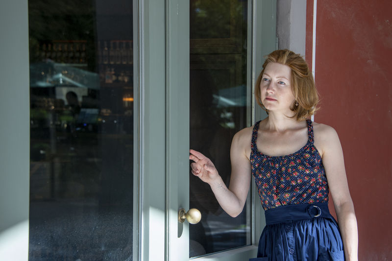 Portrait of young woman standing against window