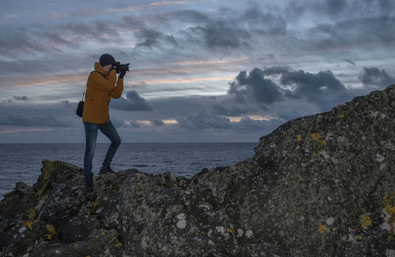 Man photographing on rock by sea against sky