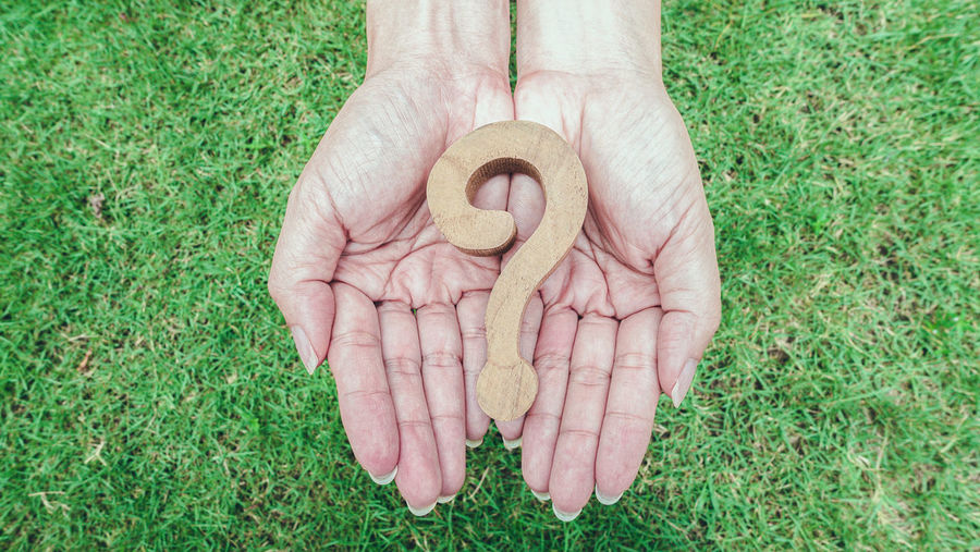 High angle view of hands holding question mark over grassy field