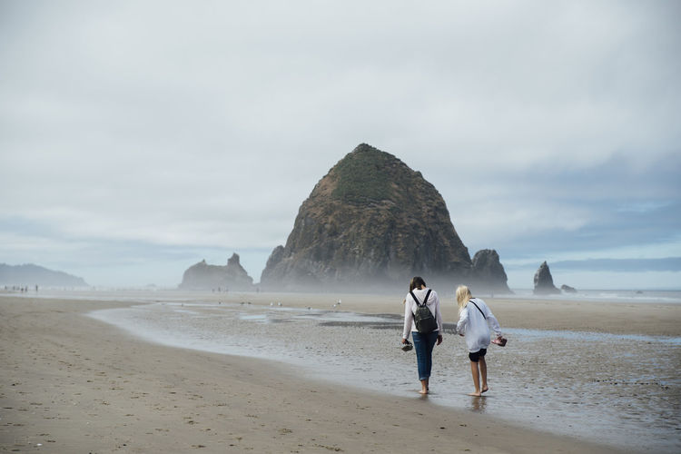 rear view of woman walking on beach against sky