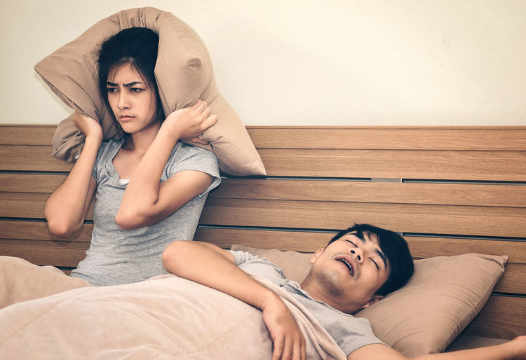 Frustrated woman sitting by man sleeping on bed at home