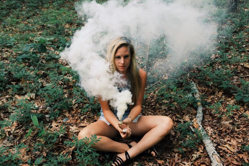 Full length of young woman holding smoke bomb while smoke emitting from it