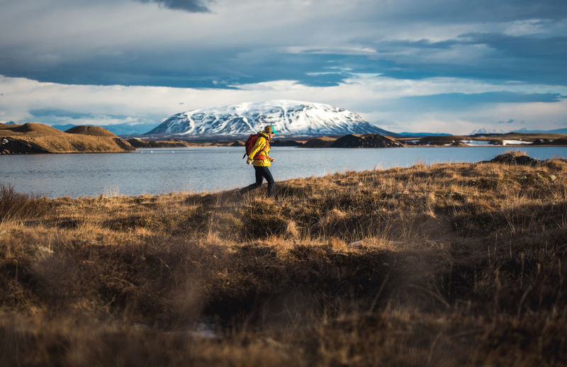 Woman walking through field next to lake with mountains in distance