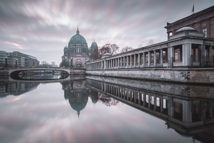 Berlin cathedral by spree river in city against cloudy sky
