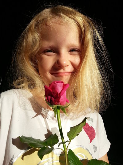 Close-up of girl holding rose and smiling against black background