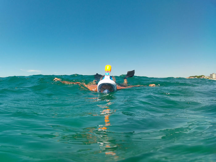Person swimming in sea against clear blue sky