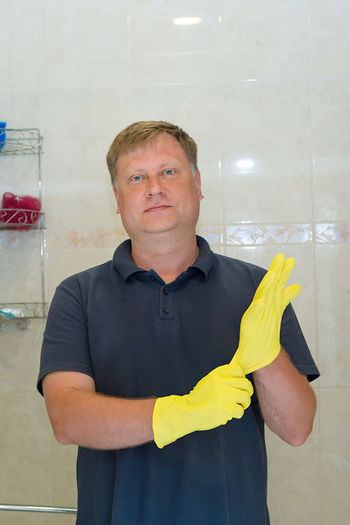 A man puts rubber gloves on his hand for cleaning bathroom.