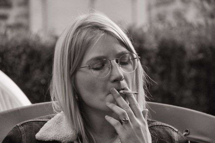 Close-up of young woman smoking cigarette while sitting on chair in yard