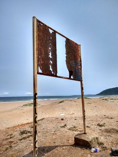Abandoned wooden post on beach against clear blue sky