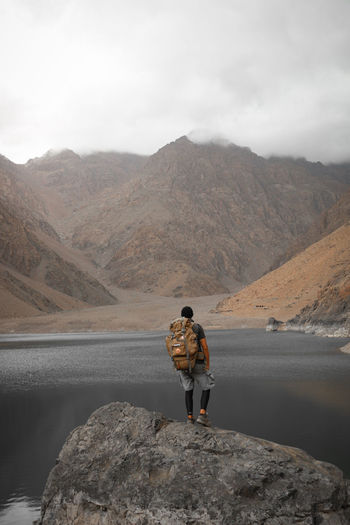 Rear view of man standing on rock by mountain against sky