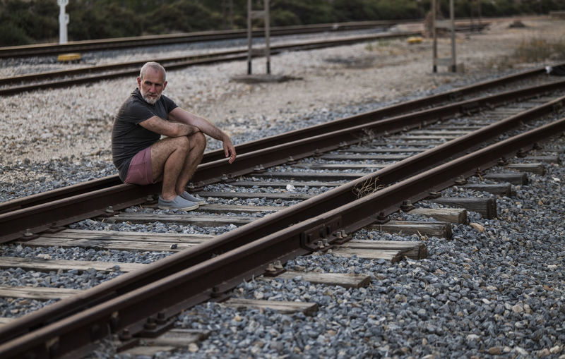 Portrait of man sitting on railroad track in summer