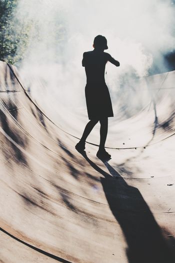Rear view of silhouette teenage boy standing on skateboard ramp