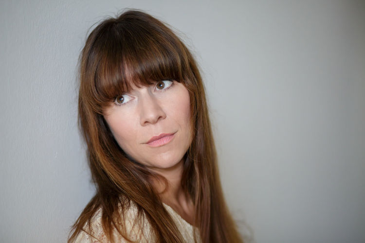Close-up of beautiful woman with bangs looking away against white background