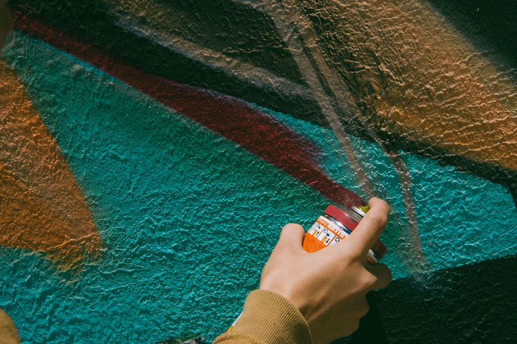 Cropped hand of person spraying paint on wall