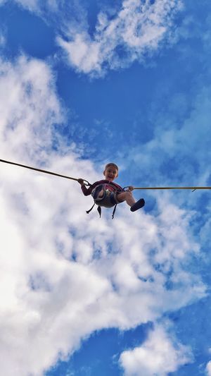 Low angle view of boy bungee jumping against sky