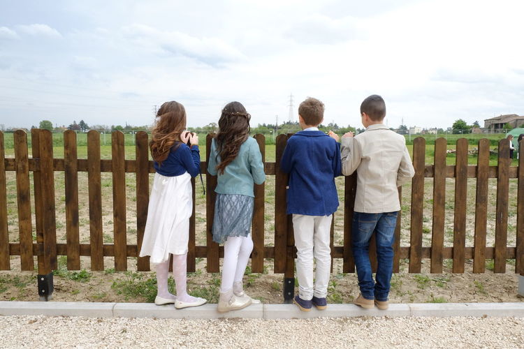 Rear view of boys and girls standing by railing against sky