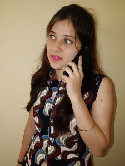 Close-up of young woman talking on phone against beige wall