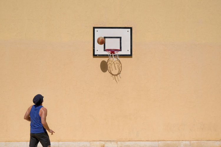 Rear view of man standing on basketball hoop against wall