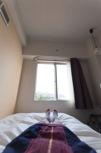 Low section of woman resting on bed against window