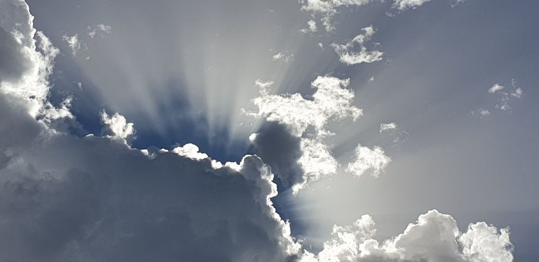 Low angle view of sunlight streaming through clouds
