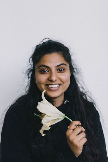 Portrait of smiling woman holding flower against white background