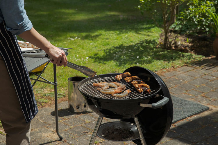 Midsection of man preparing food on barbecue grill in yard