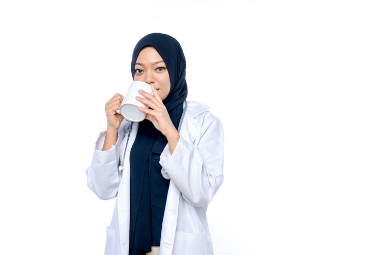 Portrait of young woman drinking coffee cup against white background
