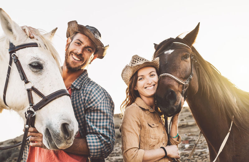 Portrait of smiling couple with horses against sky
