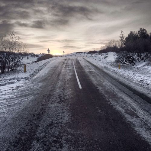 Snow covered road amidst field against sky during winter