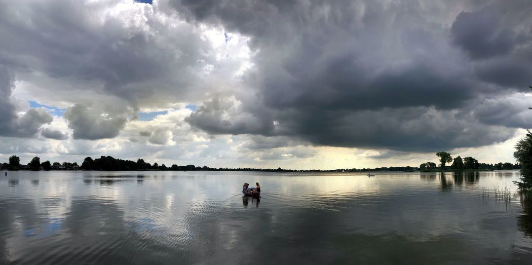 Panoramic view of silhouette people on lake against sky