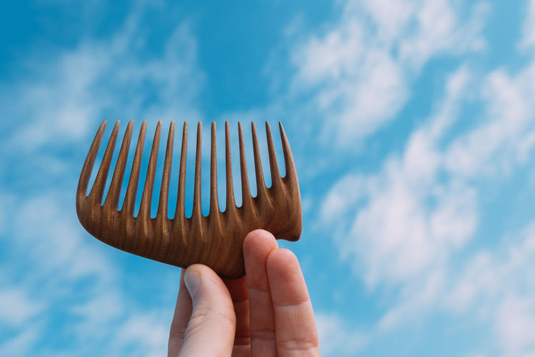 Close-up of hand holding comb against sky